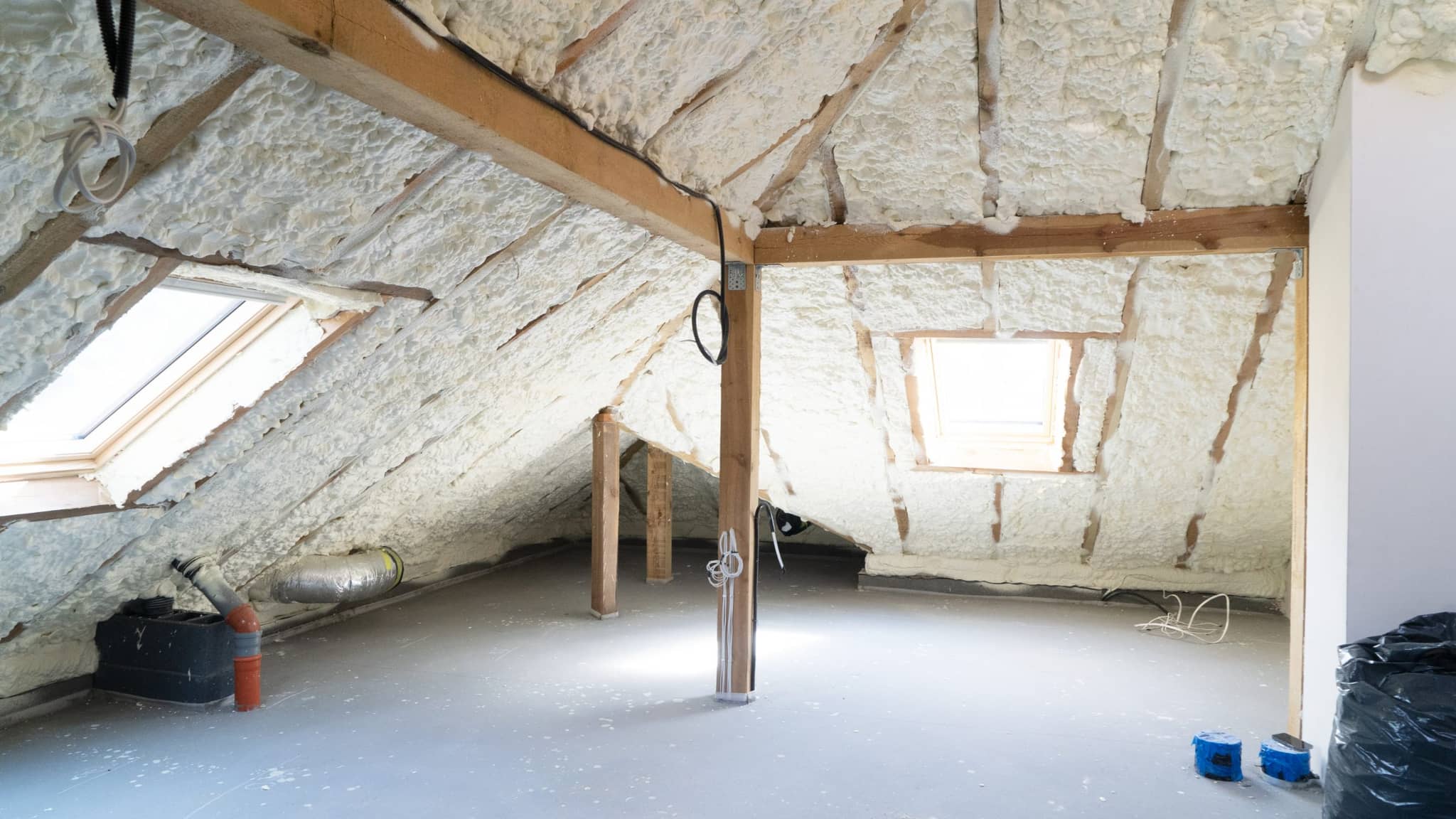 Attic with spray foam insulation between the roof rafters, two roof windows and a bare floor