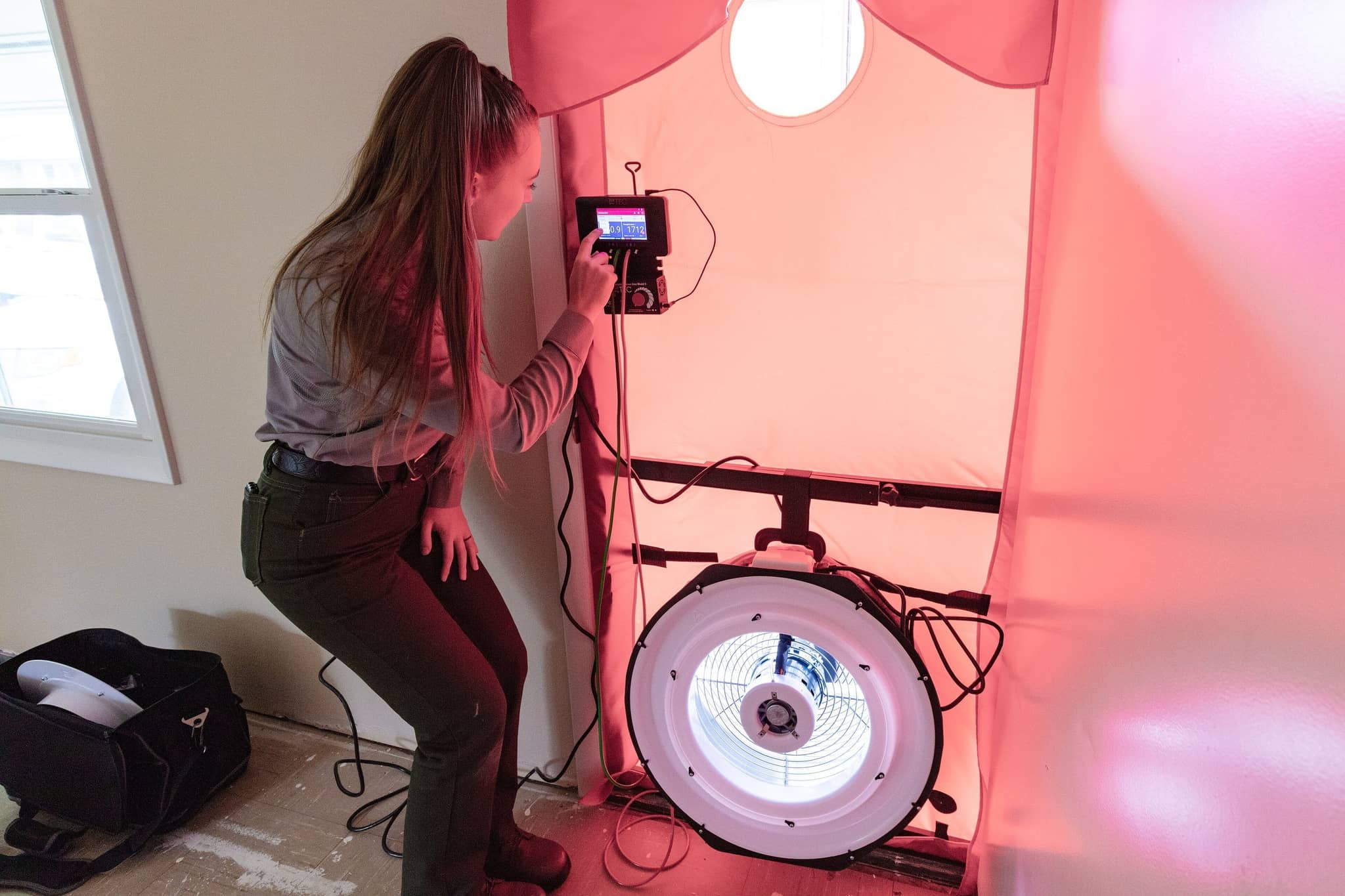 Technician reading the gauge on a blower door fan set in a doorway